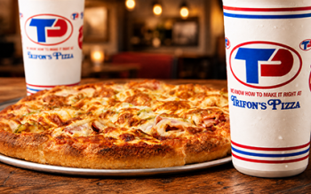 pizza on a metal pan with Trifon’s Pizza drink cups on a rustic restaurant table.